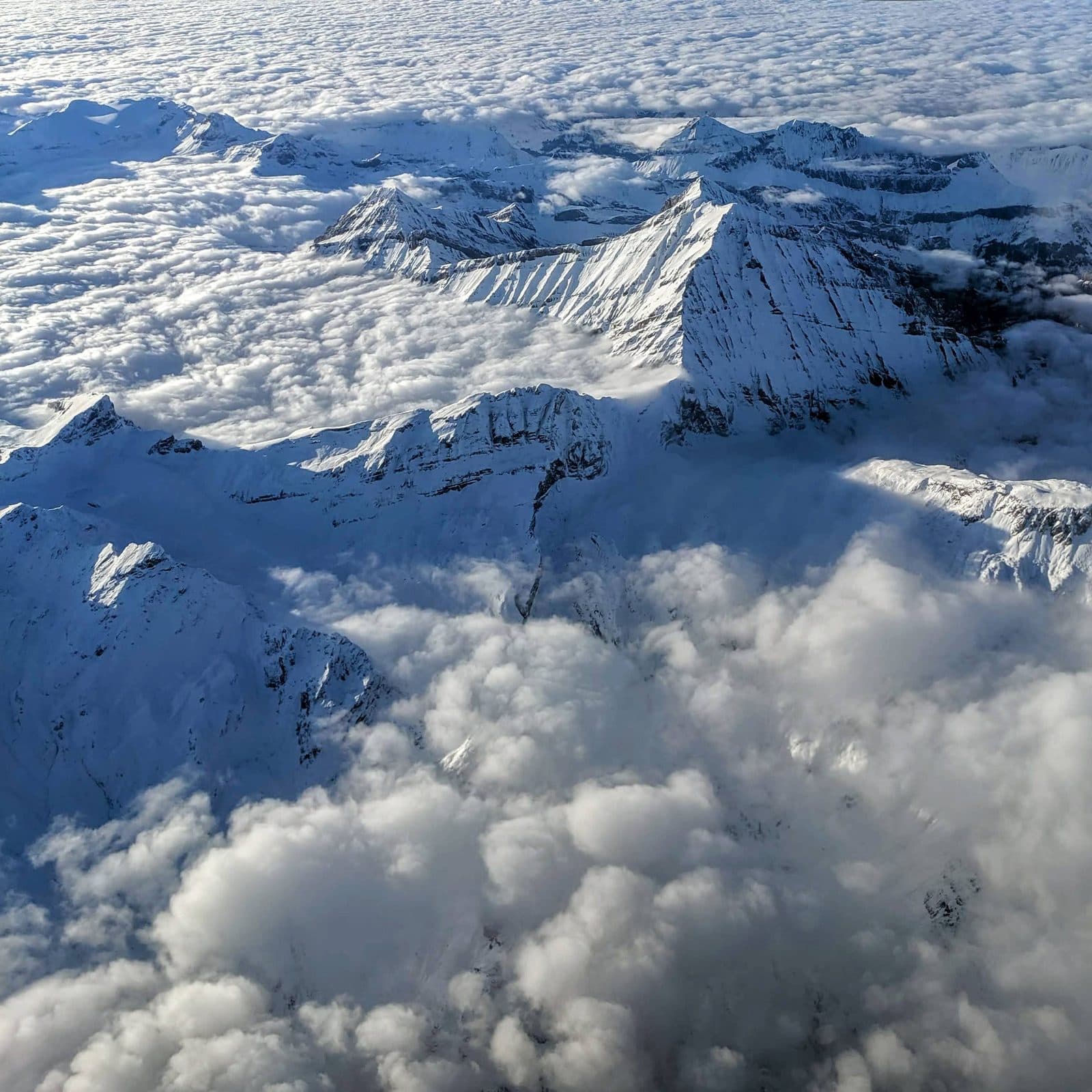 Snow covered mountains rising through the clouds, seen from a plane