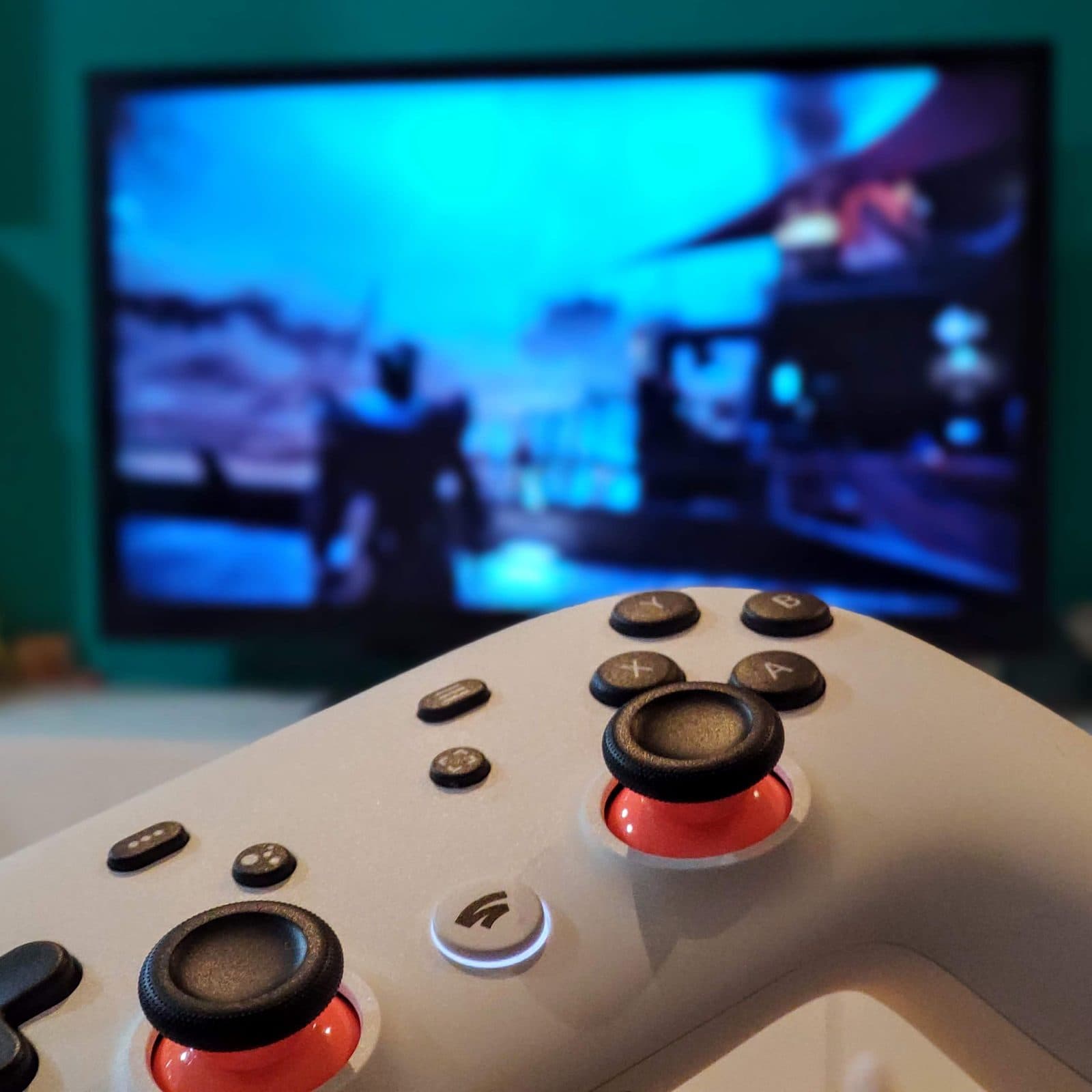A Stadia controller in the foreground, with a game playing on the TV behind it